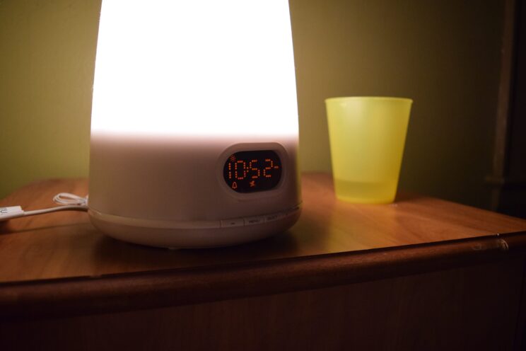 Digital alarm clock with light and a tumbler on a bedside table