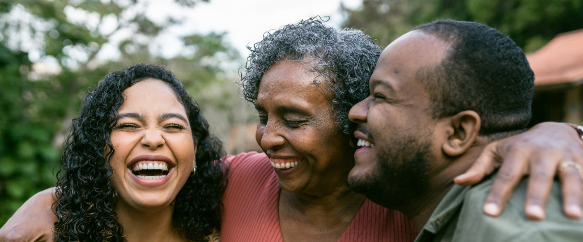 Group of three people hugging and smiling outdoors.