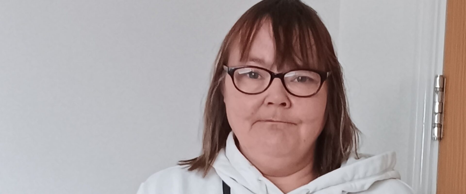 Woman with glasses in a white hoodie smiling.