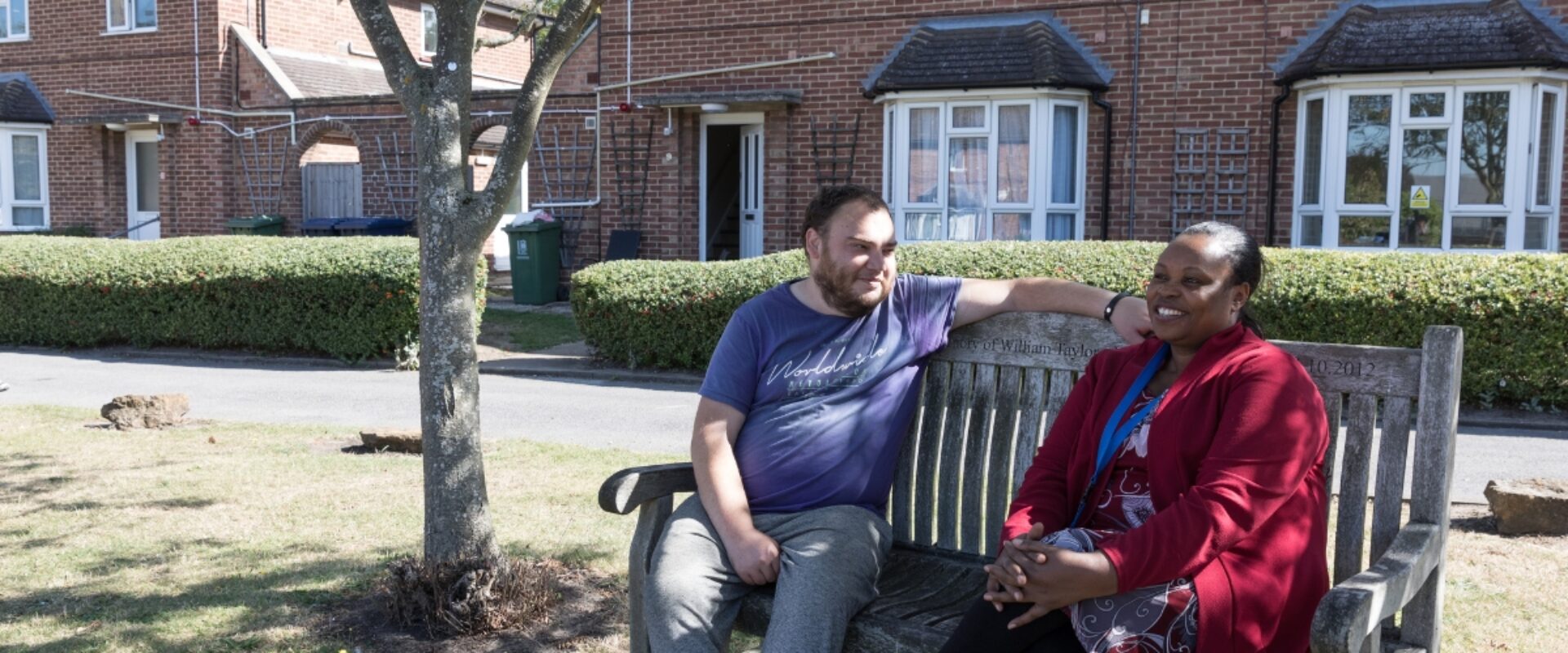 Community housing resident speaking with a visitor on a bench outdoors.