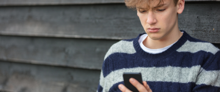 Young boy in striped jumped, using his phone looking worried.