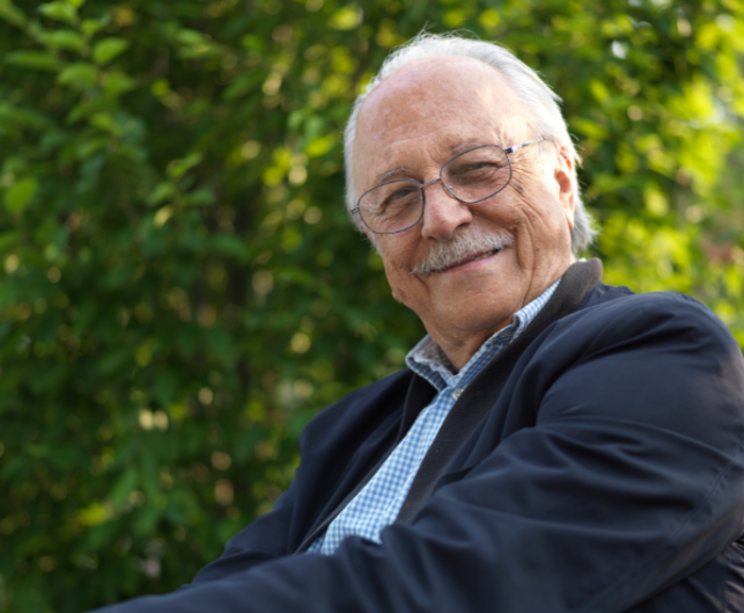 elderly man with glasses, sat outside smiling.