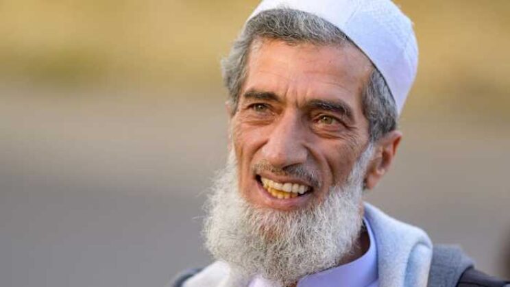 Man with grey hair and grey beard smiling outdoors.