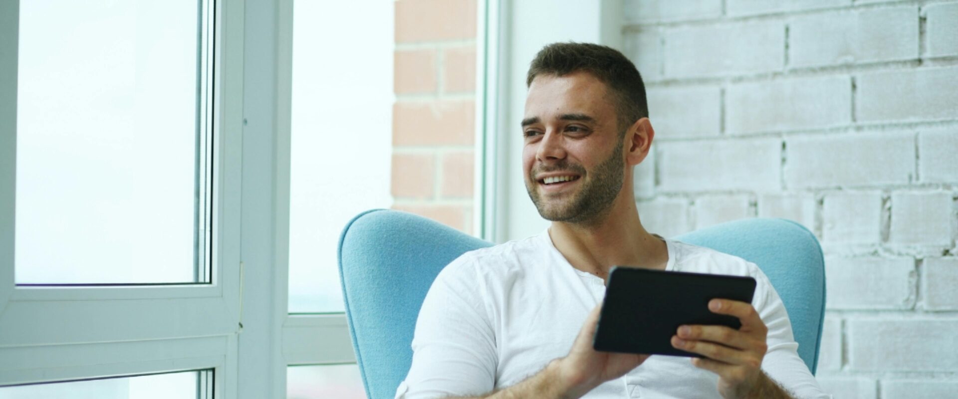 Man in white shirt smiling as he sits in chair using a mobile phone.