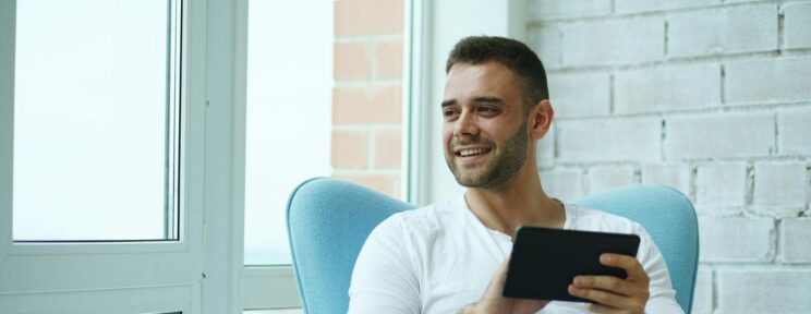 Man in white shirt smiling as he sits in chair using a mobile phone.
