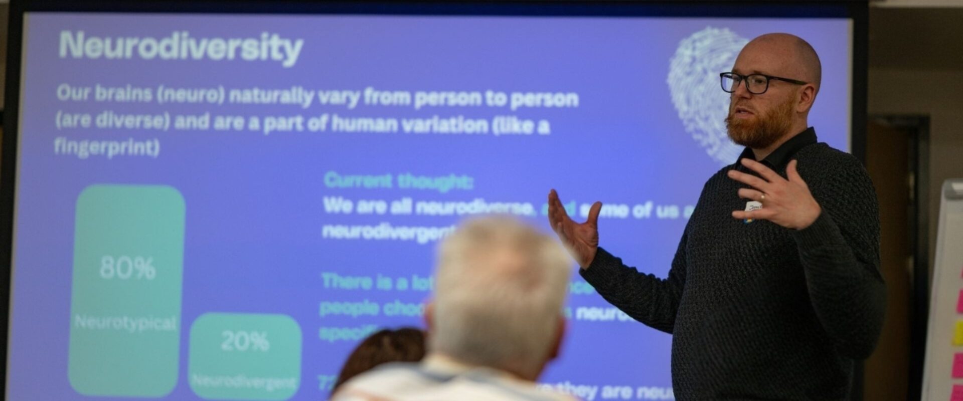 Response employee with glasses and dark jumper, speaking to people about Neurodiversity.