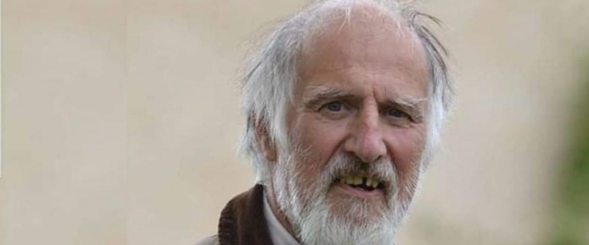 Elderly man with grey hair stood outdoors.