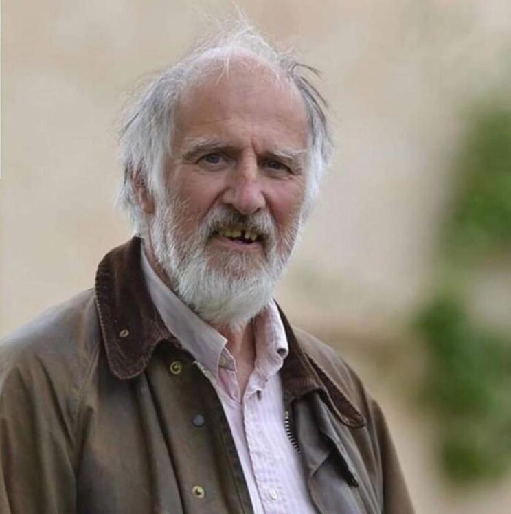 Elderly man with grey hair stood outdoors.