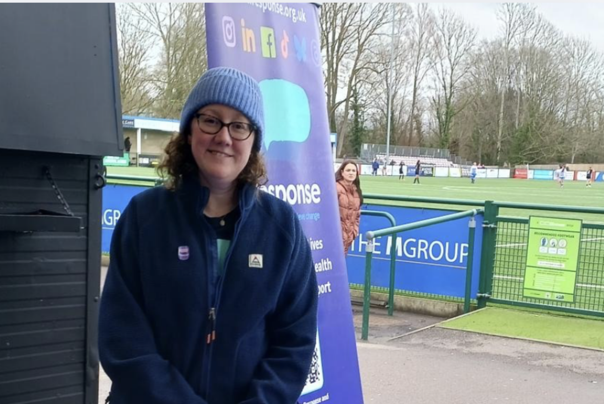 A Response colleague wearing a hat stands at a Response fundraising stall by the Oxford City Football Club pitch.