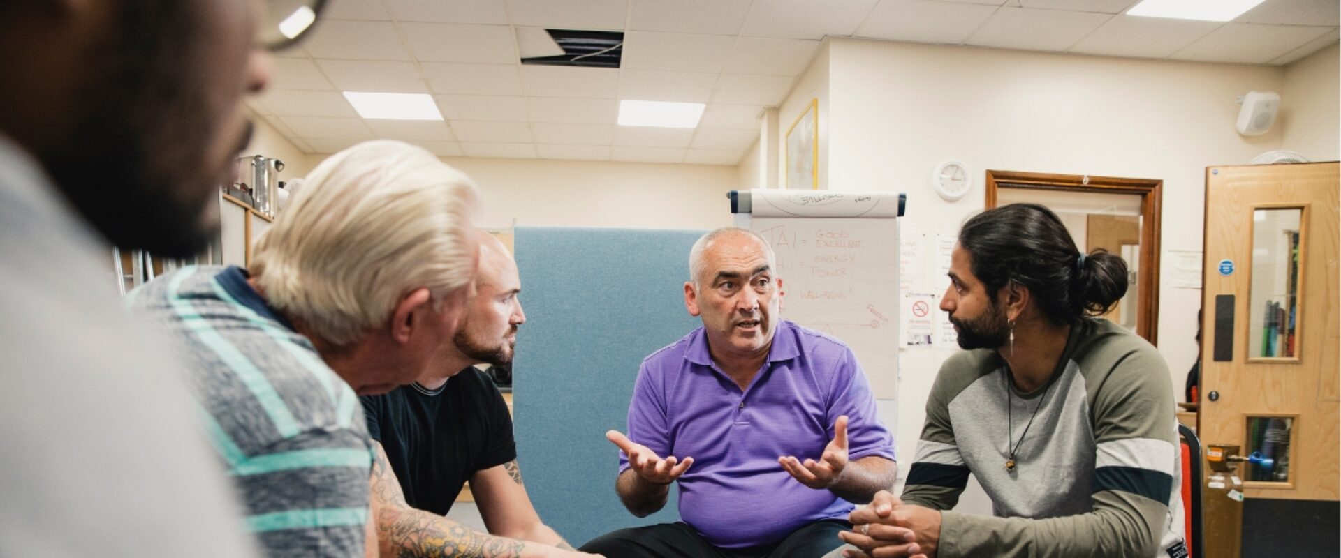 Group of people sitting down talking to eachother indoors.