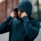 Young man in black hoodie with hood up, stood outdoors.