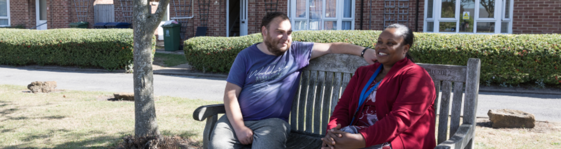 A man and woman sitting on a bench in the sunshine outside a row of Response houses.