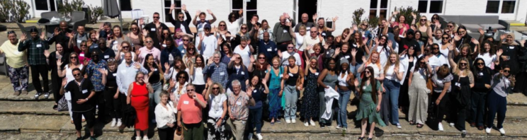 A drone photo of a large group of Response staff waving to the camera outside a white painted building on a staff training day.