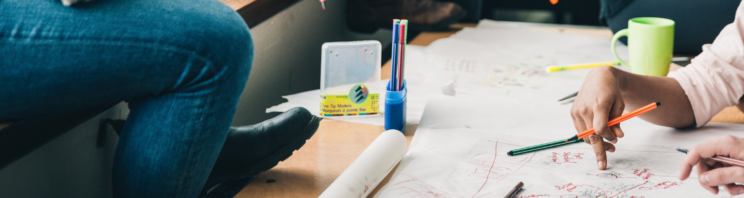 Close up image of students working together around a table and writing on a large sheet of paper.