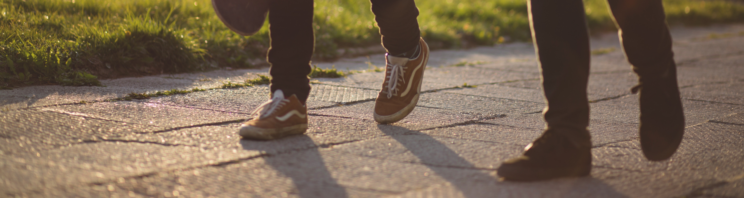 Two pairs of people's feet wearing trainers walking on a path together.