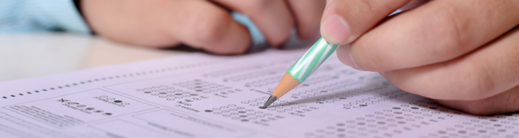 Close up photo of exam paper with a person writing their answers in pencil.