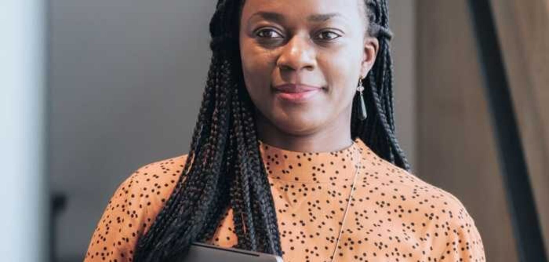 Woman in orange top, holding a laptop and smiling.