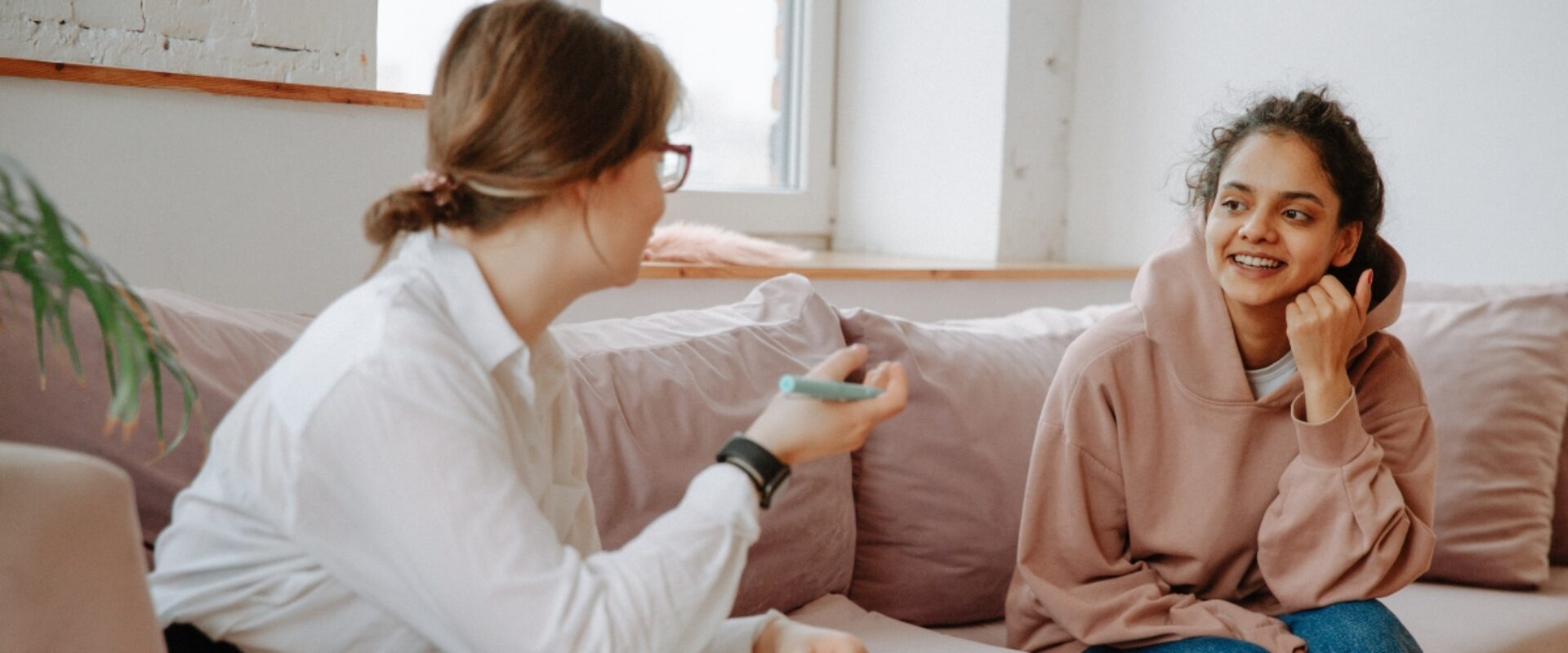 A young woman and older woman on a pink sofa smiling and talking.