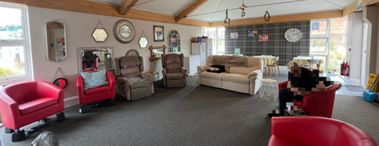 A spacious communal lounge with an assortment of armchairs and sofas, decorative mirrors, exposed wooden beams, and large windows letting in natural light.