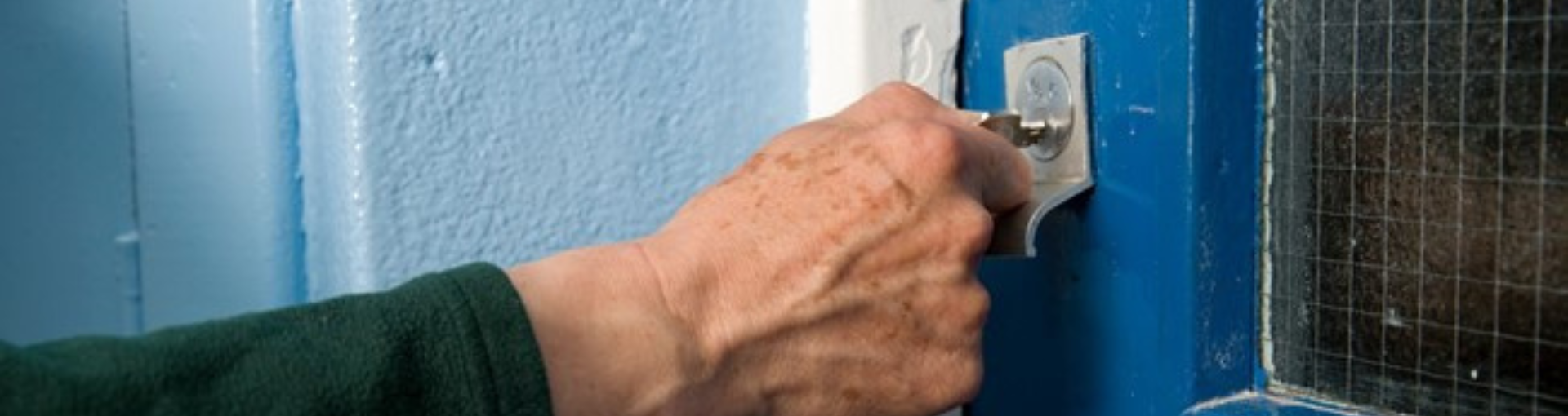 A close-up of a person's hand turning a key in a door lock.