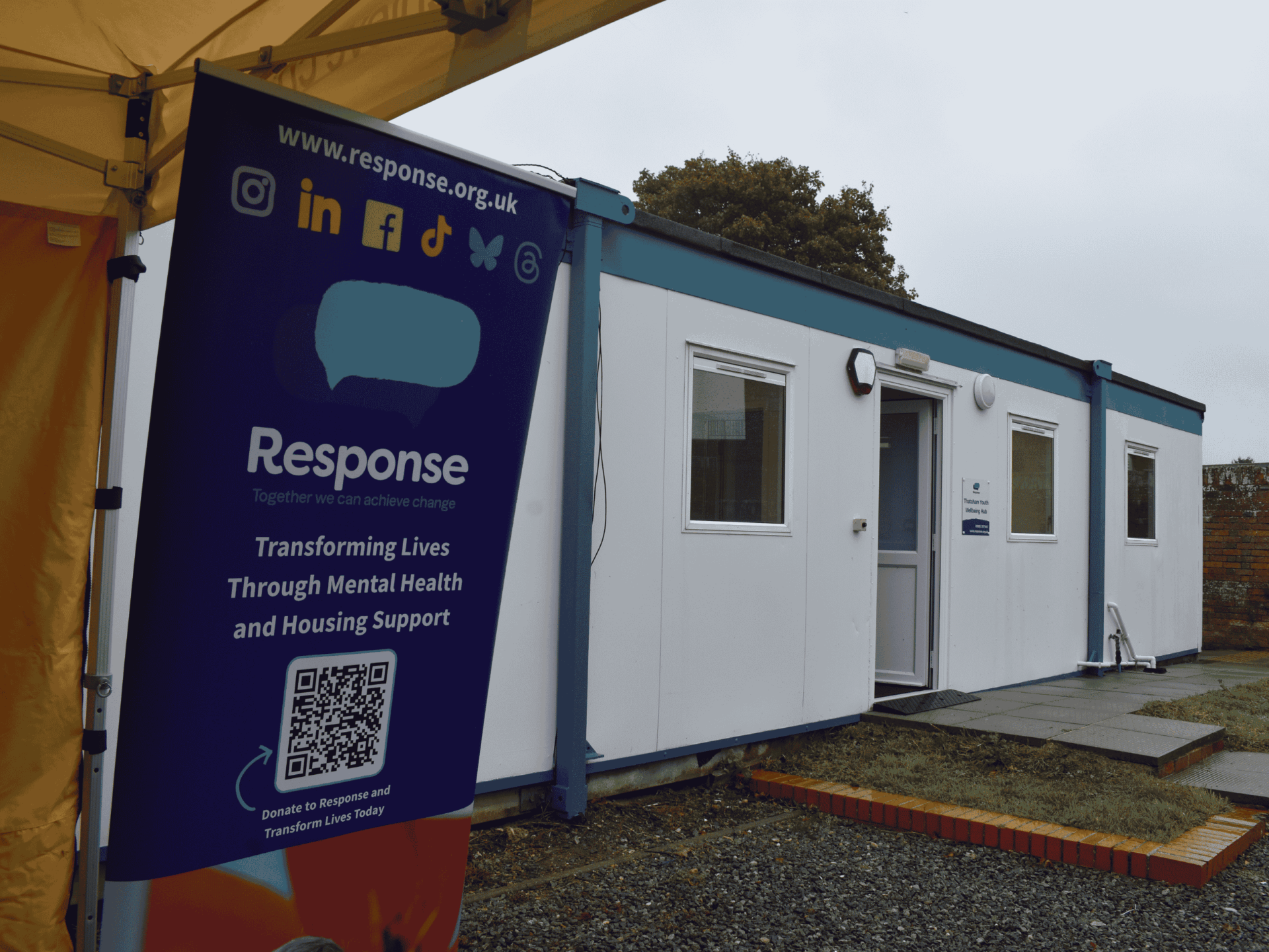 Photo of the Thatcham Wellbeing Hub, a small white building with a Response banner outside in the garden area.