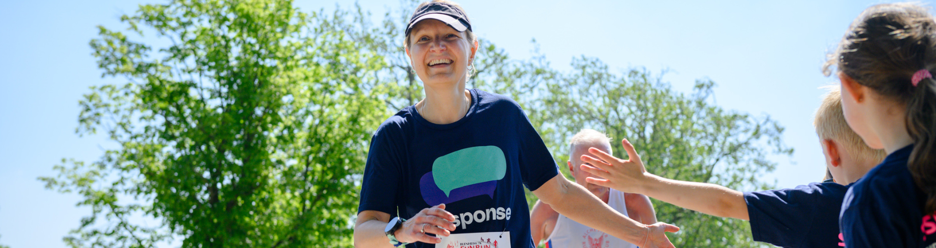 A Response runner smiling as a child high-fives her during a sunny outdoor fun run.