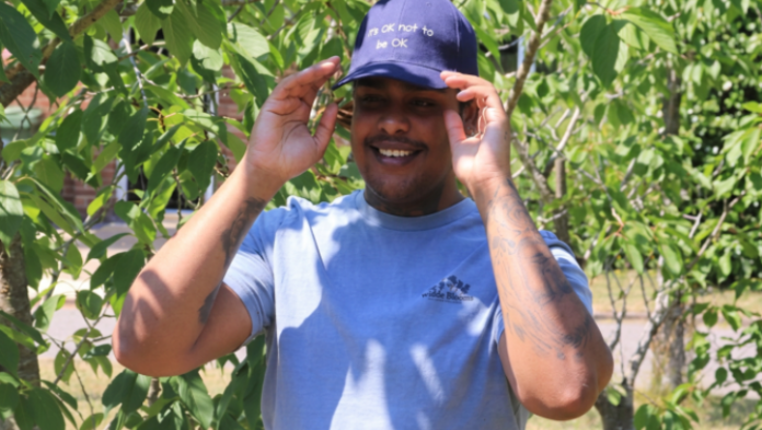 Image of a man wearing a navy blue Response baseball cap, he stands in front of a tree in the sunshine.