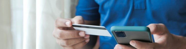 Photo of person in blue top holding a bank card in one hand and a mobile phone in the other.