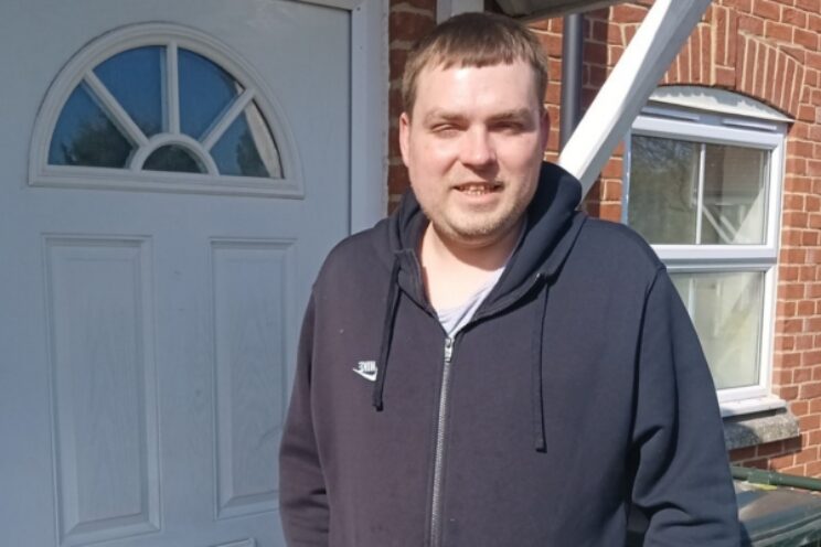 Response resident, Scott, in black hoodie stood in front of white door.