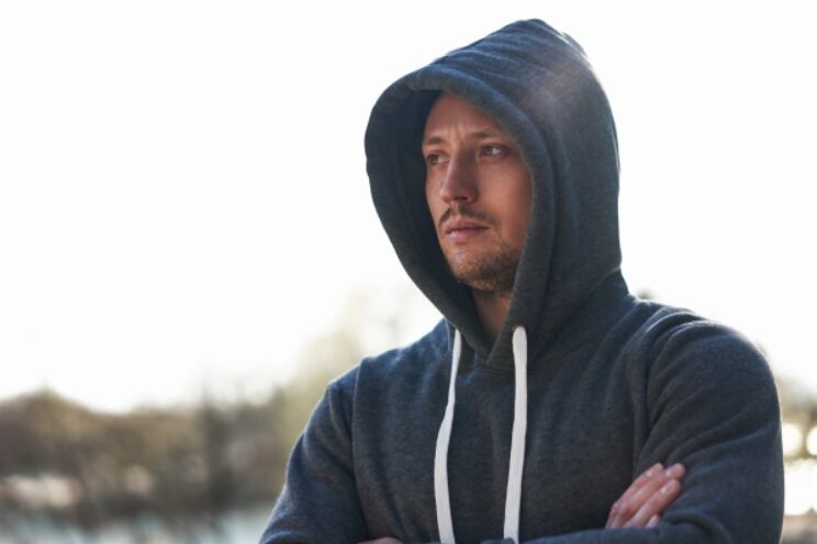 Man in grey hoodie stood outdoors.