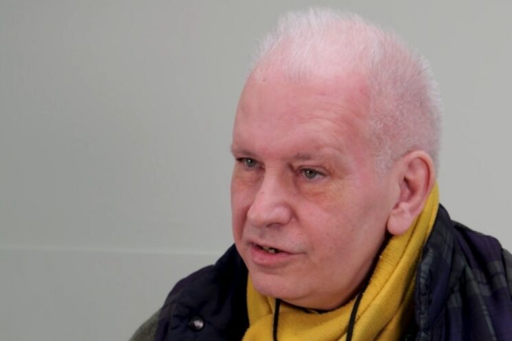 Photo of man in black coat and yellow scarf.